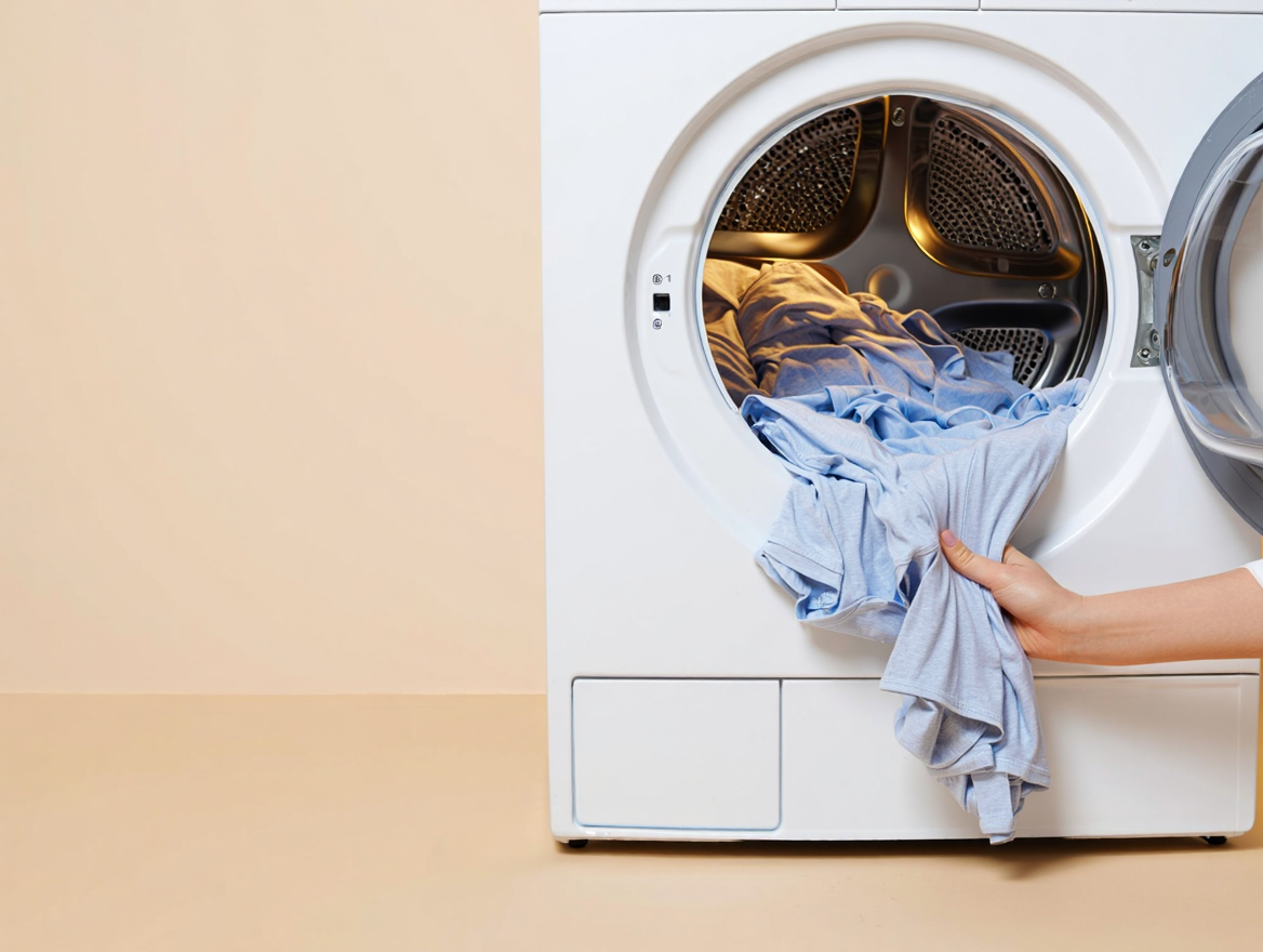 Dryer set to Low/Delicate with a small load of cotton T-shirts; a hand removing a tee while still slightly damp.